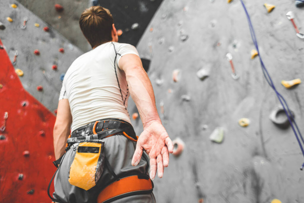 Sportsman climber is looking on steep rock, climbing on artificial wall indoors. Extreme sports and bouldering concept - Photo, image