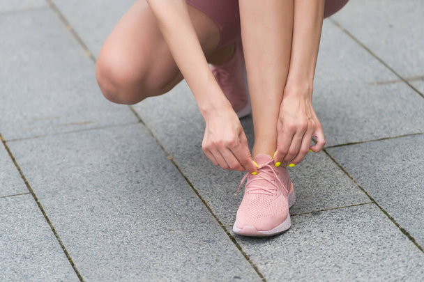 Comfort and style in balance. Female hands lace sport shoe. Tying shoelaces. Womens running shoe. Gym shoe on arena ground. Athletic footwear. Running shop. Fitness and training. Healthy lifestyle - 写真・画像