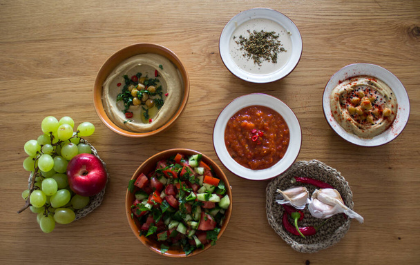A Közel-Kelet autentikus étele. Tányér humusz, falafels, pitakenyér, harissa szósz, tahini, friss saláta és gyümölcsök a fa asztalon. Hagyományos ételek Izrael top view fotó. Gyönyörű étel kép másolási hellyel. - Fotó, kép