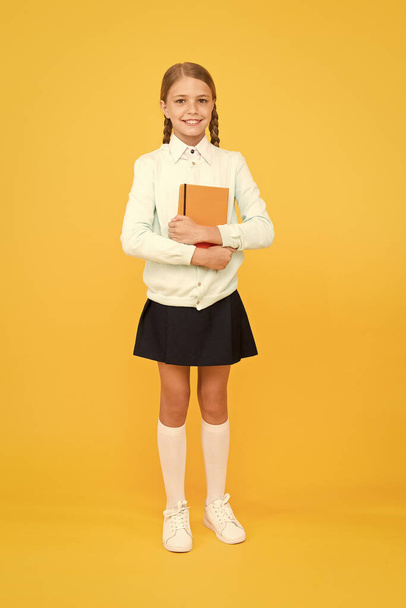 A firm knowledge base for future. Adorable small girl holding book on yellow background. Cute little child with book knowledge in hands. Knowledge and skills. Knowledge day or September 1 - Foto, imagen