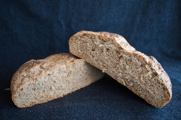 Volkoren brood met chiazaad. Rond brood doormidden gesneden met zwarte ondergrond - Foto, afbeelding
