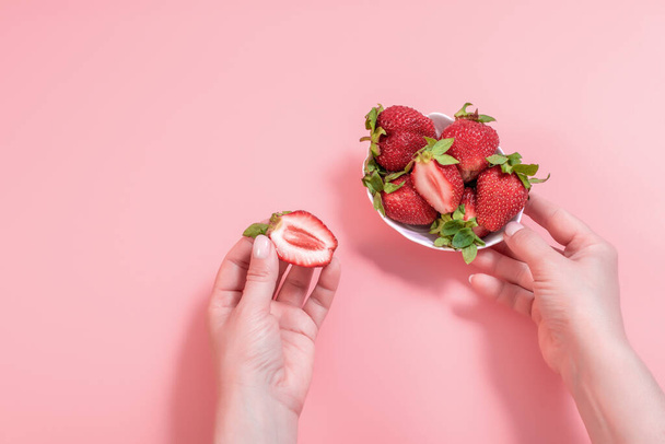 Close-up fresh peeled strawberry in white bowl on pink background. A woman's hand takes strawberries from a bowl Summer healthy eating concept. - Φωτογραφία, εικόνα