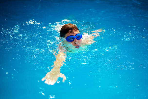 Little boy athlete swims in the pool by the crawl. The concept of training and childrens sports - Фото, изображение