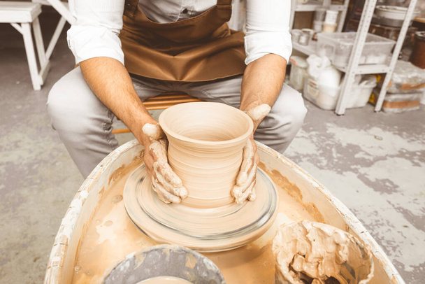 A young male potter works in his workshop on a potters wheel and makes clay products. Close-up of hands - Fotoğraf, Görsel