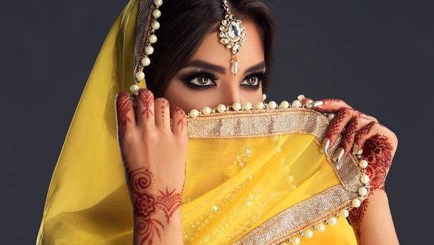Hermosa chica india. Joven modelo de mujer hindú con tatoo mehndi y joyas kundan. Traje indio tradicional saree amarillo. Mujer india o musulmana cubre su cara
. - Foto, Imagen