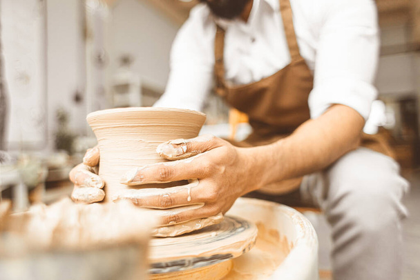 A young male potter works in his workshop on a potters wheel and makes clay products. Close-up of hands - 写真・画像