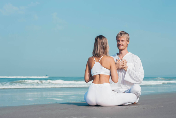 guy and girl in white clothes are sitting on the ocean and holding hands - Photo, Image