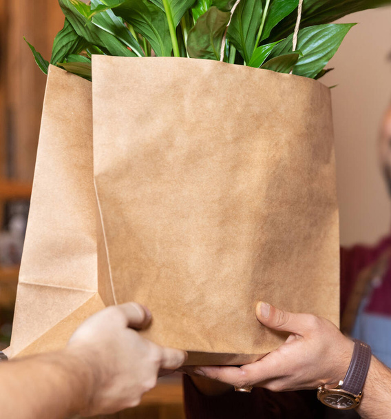 顧客に買い物袋を与える庭の店の労働者、内部の植物 - 写真・画像