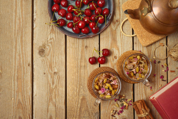 Dry herbal tea with fresh cherries on wooden table. Healthy lifestyle concept. View from above - Photo, Image