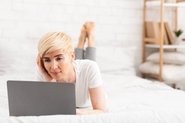 Успешная женщина лежит на кровати и работает на ноутбуке
 - Фото, изображение