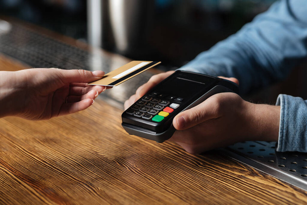 Современная бесконтактная оплата счета в пабе. Клиент держит кредитную карту, бармен холдинг терминал
 - Фото, изображение