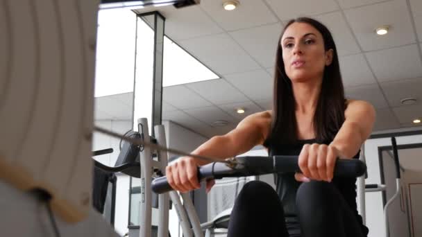 beeldmateriaal van mooi brunette vrouw uit te werken op sportschool op roeien machine - Video