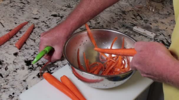 Carrot Being Peeled by Male Hands with a Green Peeling Utensil. Ο αποφλοιωτής τροφίμων που χρησιμοποιείται από καυκάσιους αρσενικούς για να ξεφλουδίσουν τα δέρματα καρότου σε ένα μπολ από ανοξείδωτο χάλυβα. Ένα πορτοκαλί βιολογικό καρότο καθαρίζεται από μια πράσινη συσκευή ξεφλούδισμα τροφίμων σε ένα μπολ. - Πλάνα, βίντεο