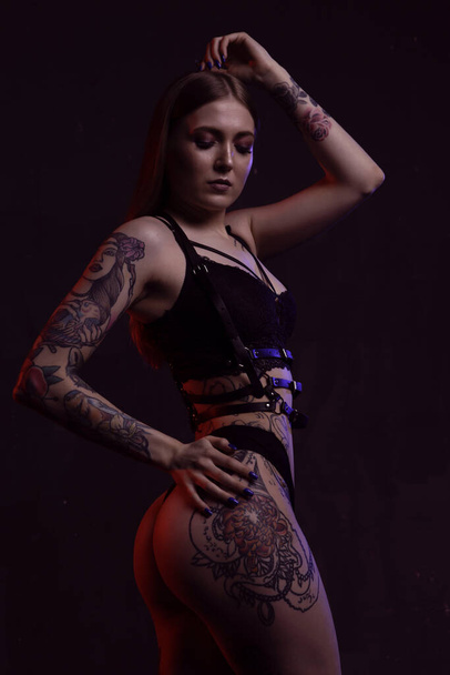 A gorgeous young tattooed model poses sexily against a dark isolated background - Фото, зображення