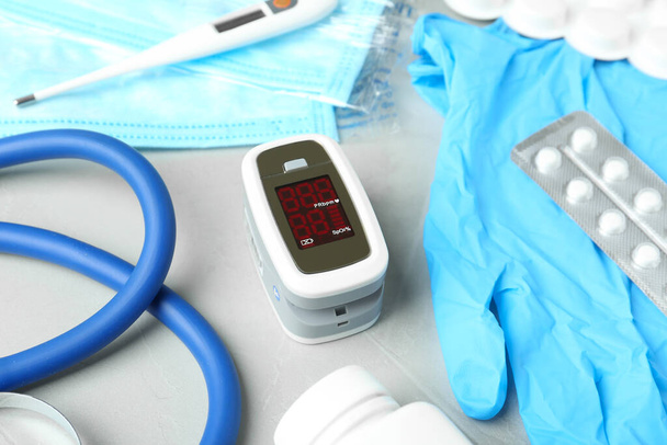 Modern fingertip pulse oximeter and medical items on light grey stone background - Фото, зображення