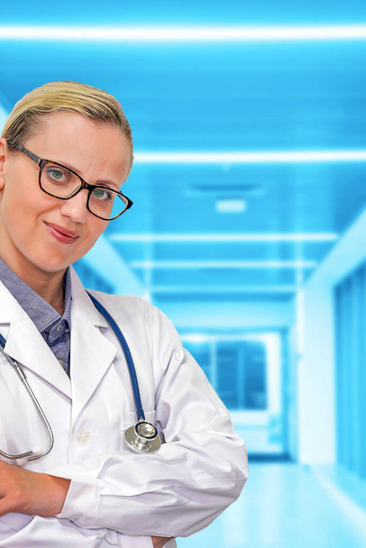 診療所のぼやけた廊下を背景に眼鏡と聴診器を持つ医師の女性。コピースペース付きの医療ウェブサイト。ヘルスケアバナー. - 写真・画像