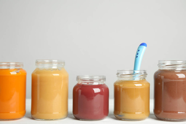 Healthy baby food in jars on white wooden table against grey background, space for text - Fotoğraf, Görsel