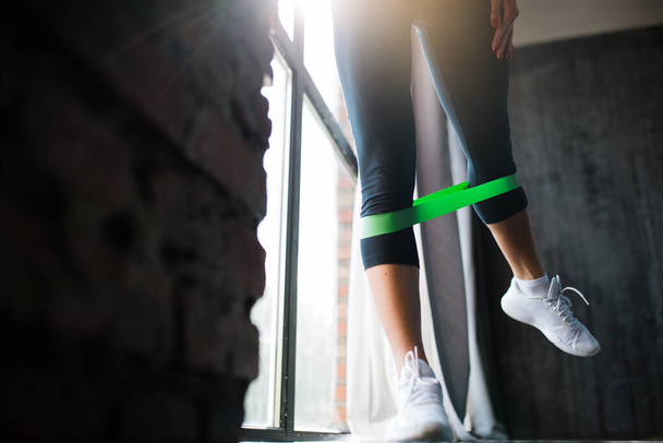Close-up of legs of athlete who put on her calves green elastic tape to strengthen the muscles of legs against a panoramic window - Photo, image