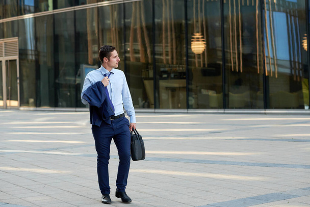 Tired young businessman with case going after work in hot weather   - Fotó, kép