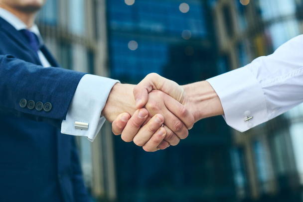Business handshake outdoor in front of office building. Partnership meeting concept. Successful businessmen handshaking after good deal.  - Foto, Imagen
