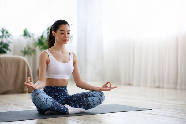 Életharmónia. Nyugodt ázsiai lány meditál Lotus pozícióban otthon - Fotó, kép