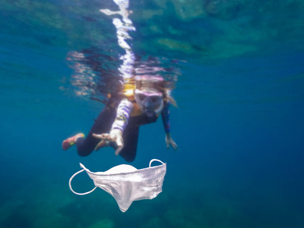 Gönüllü kız mayo ile şnorkelle yüzüyor ve okyanusta maske çöpü topluyor. Kumsalda çöp toplayan bir temizlikçi. Çöpleri temizliyorum. Gönüllü olmak ve koronavirüs konseptini geri dönüştürmek. - Fotoğraf, Görsel
