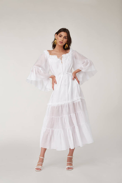 Beautiful woman fashion model makeup brunette hair perfect body shape tanned skin wear clothes summer collection organic long white silk dress stylish sandals shoes, accessory jewelry earrings date. - Zdjęcie, obraz