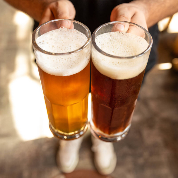 Homem segurando cerveja branca e preta lado a lado
 - Foto, Imagem