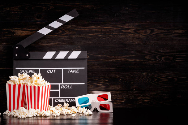 Clapper board, stripped boxed of popcorn and 3D glasses front view on dark background - Photo, Image