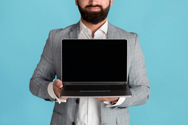 Homme d'affaires méconnaissable tenant un ordinateur portable avec écran blanc sur fond bleu, espace pour votre conception - Photo, image
