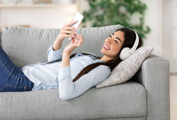 Asian girl enjoying listening music on smartphone with wireless headphones at home - Photo, image