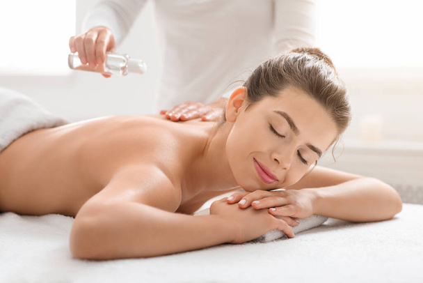 Massagetherapeutin gießt Öl auf junge Frau - Foto, Bild