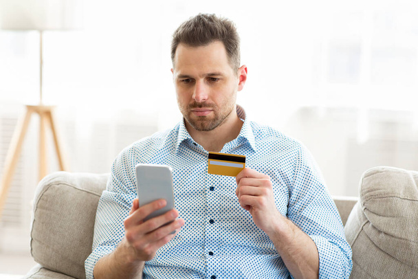 Serious man holding smartphone and credit card - Foto, afbeelding