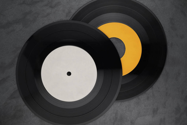 Two 7-inch single vinyl records with yellow and white labels on black slate background. Top view - Photo, Image