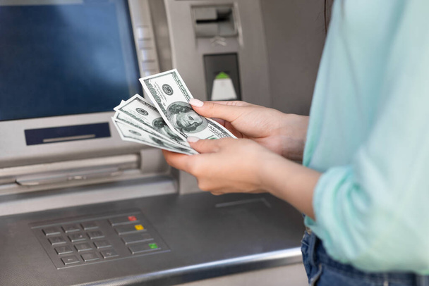 Nierozpoznawalna kobieta licząca pieniądze w dolarach w pobliżu bankomatu - Zdjęcie, obraz