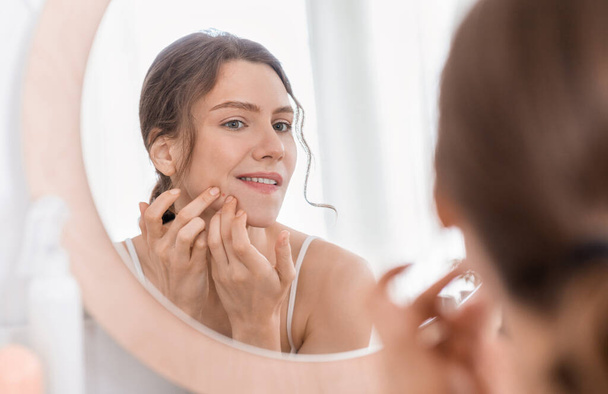 Menina olhando no espelho e toque Pimple
 - Foto, Imagem
