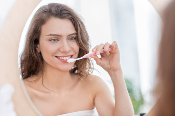 Young woman brushing teeth in bathroom at home - Фото, изображение