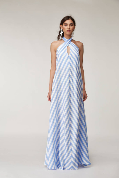 Sexy fashion model beautiful woman pretty face natural makeup, tanned skin body  wear summer collection clothes style for romantic date light silk in white blue stripes long midi dress earrings. - Φωτογραφία, εικόνα