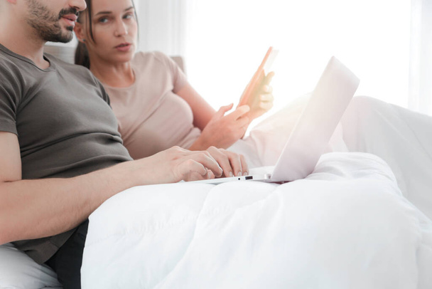 寝室から働くカップル,ラップトップコンピュータを使用して男,ベッドの上に横たわっている間にデジタルタブレットを使用して女性,情報とオンラインショッピングを検索,オンラインビジネスのためのソーシャルメディア,フォームホーム - 写真・画像