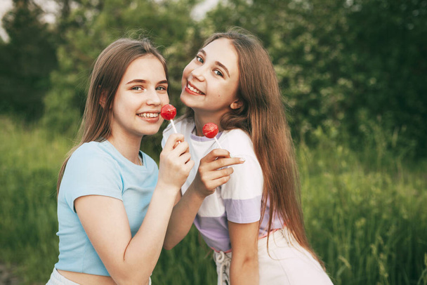 Two happy teenage girls holding a bright red lollipop candy. - Foto, imagen