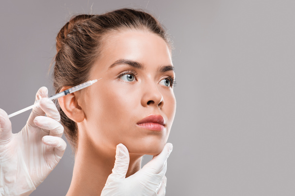 Young beautiful woman getting botox injection over grey background - Foto, Imagem