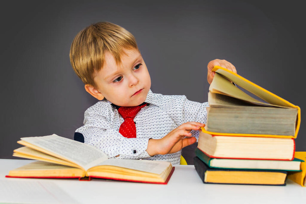 menino pré-escolar sério na mesa com livros em um fundo cinza - Foto, Imagem