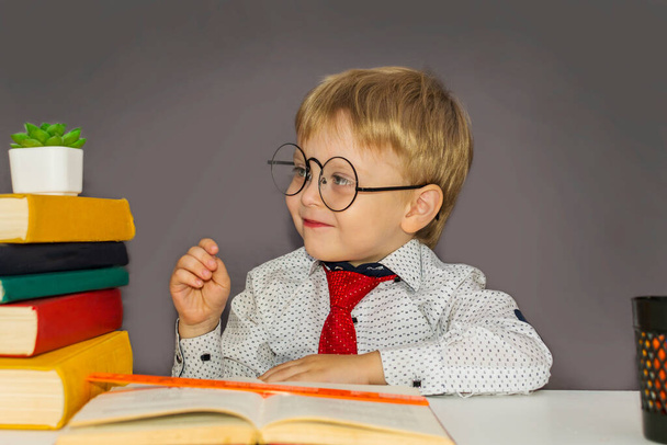 cute boy with glasses sitting at a Desk. Blond nerd with glasses. - Fotografie, Obrázek