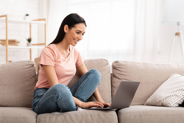 Woman using laptop phone sitting on sofa - Zdjęcie, obraz