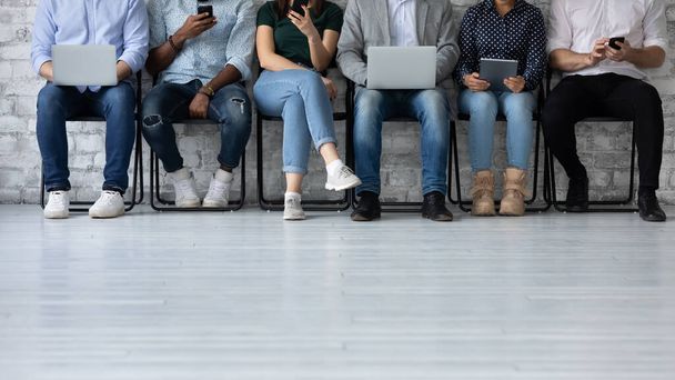 Six multiethnic young people sit in queue holding electronic devices - Φωτογραφία, εικόνα