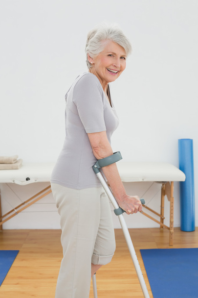 Side view of a smiling senior woman with crutches - Foto, afbeelding