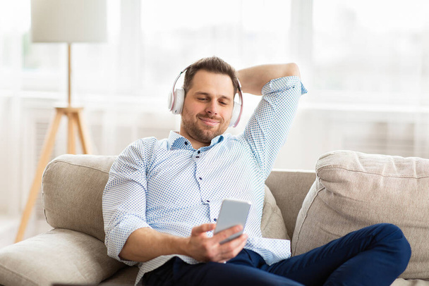 Happy man listening to music sitting on sofa - Фото, зображення
