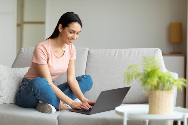 Успешная фрилансер девушка с ноутбука компьютер сидит на диване в помещении
 - Фото, изображение