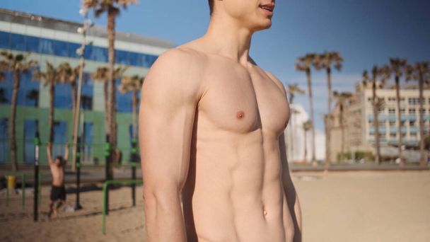 Close up young sporty man with naked torso resting resting after workout on city beach - Foto, imagen