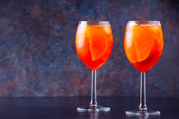 Aperol spritz cocktail in glass on dark background. Two glasses of aperol spritz with sliced orange. Summer cocktail in glass. Copy space - Fotoğraf, Görsel
